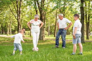 Happy family playing soccer on summer meadow. Grandparents with his little cute grandchildren are having fun and playing football on green grassy lawn. Active family play soccer in their leisure time